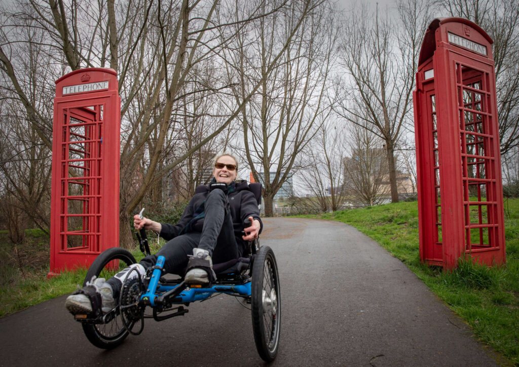 Jamie Lawson at an All Ability Club - cycling on her adapted trike between two red phone boxes